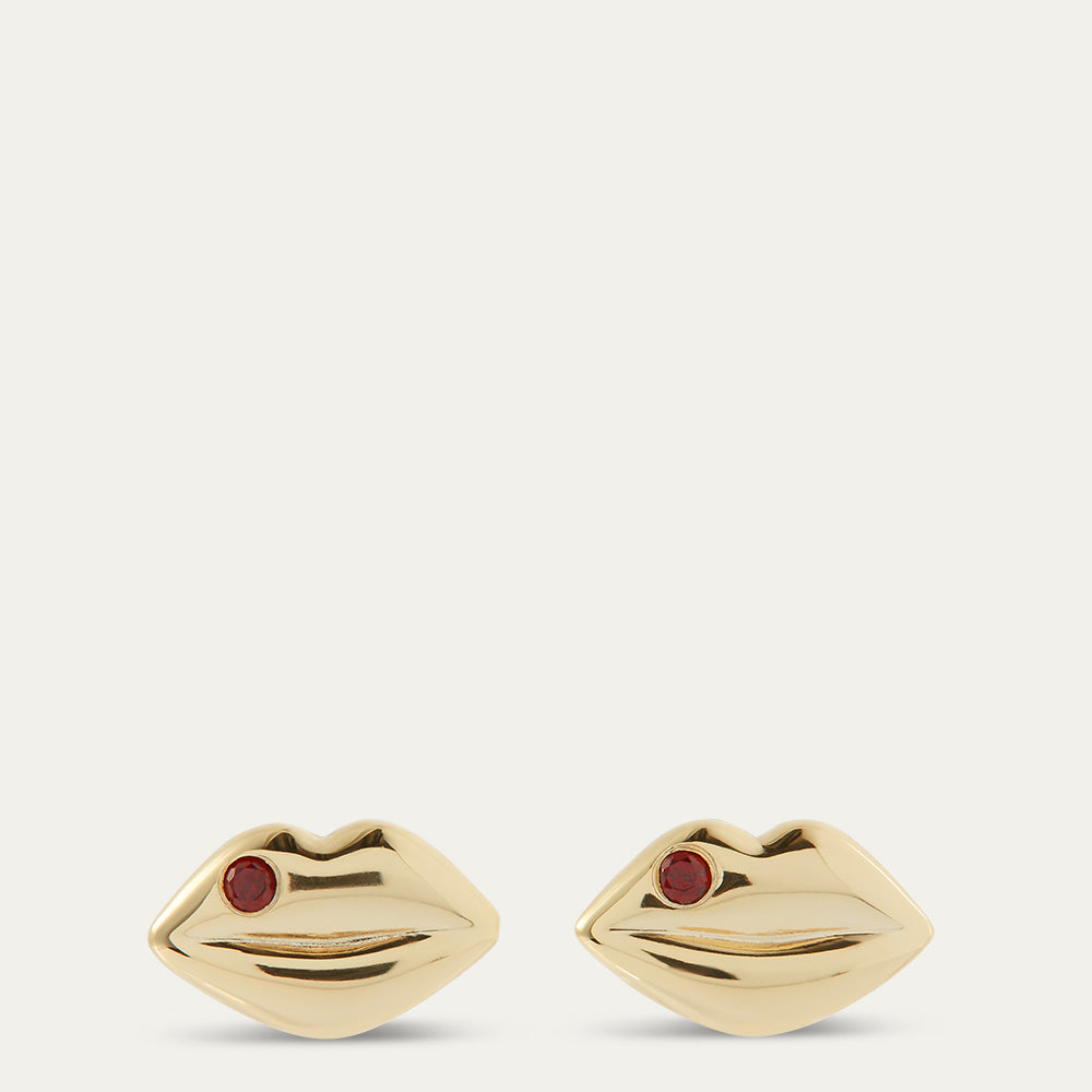 Gold earrings shaped like lips with red gemstones on a white background