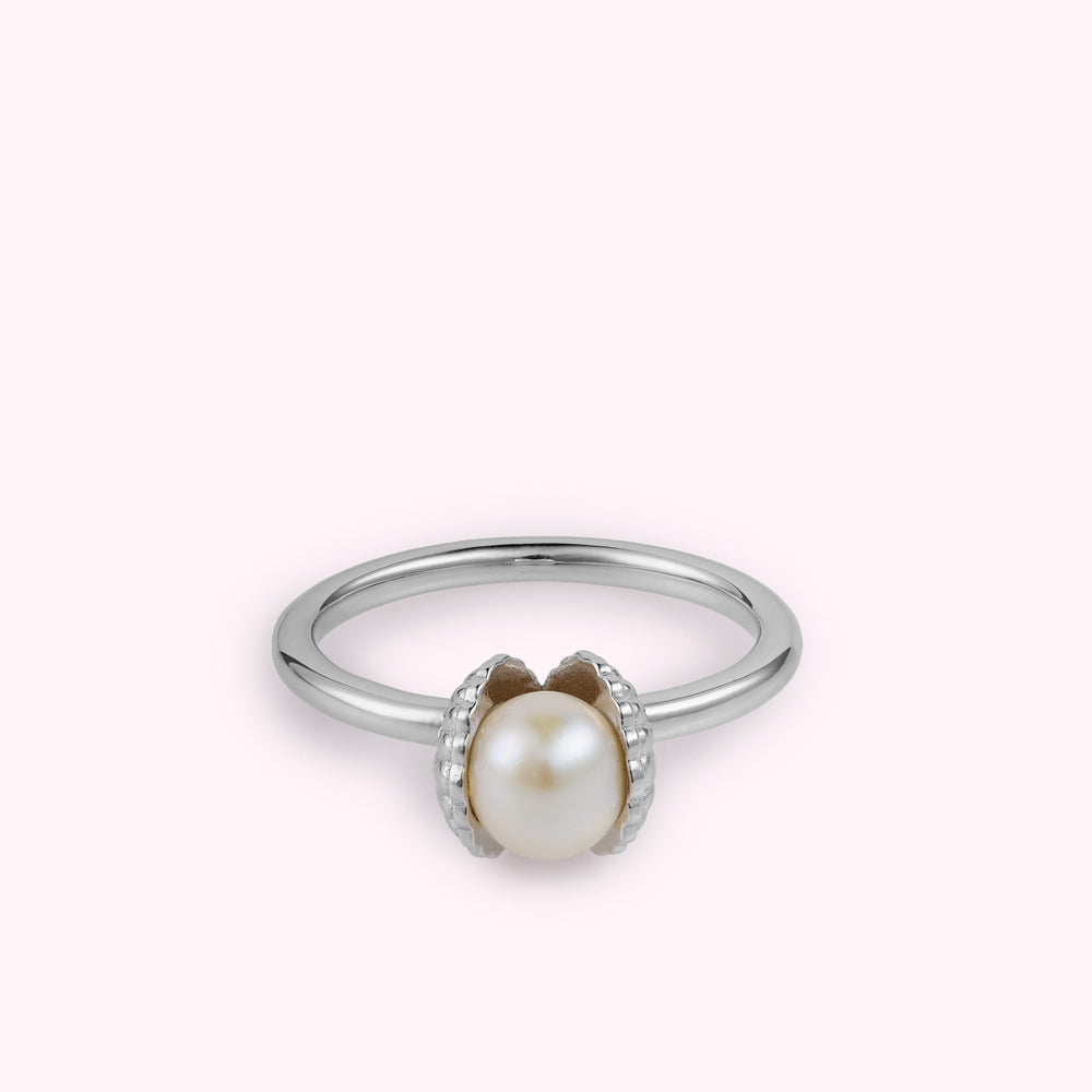 Sterling silver shell shaped ring with a freshwater pearl flat on a white surface.