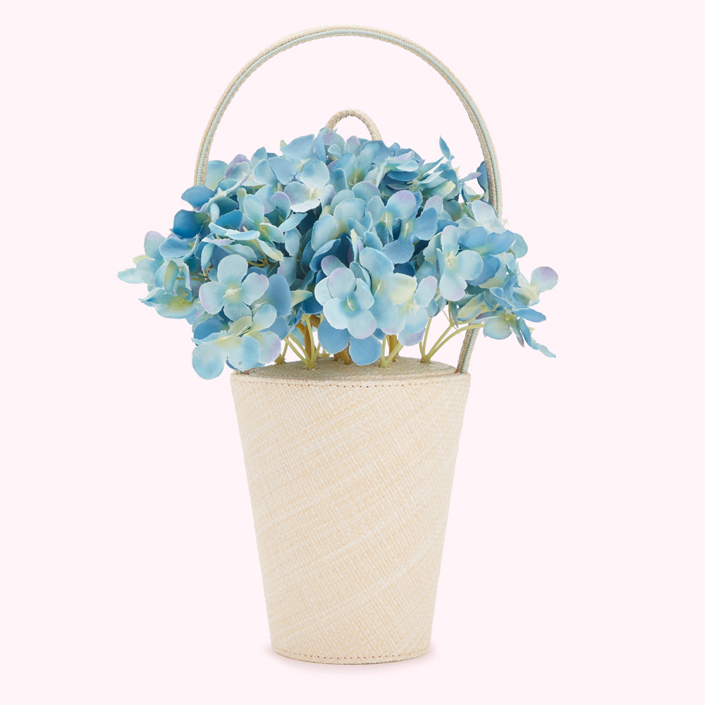 A bouquet of light blue hydrangeas on a cream-colored woven basket handbag.