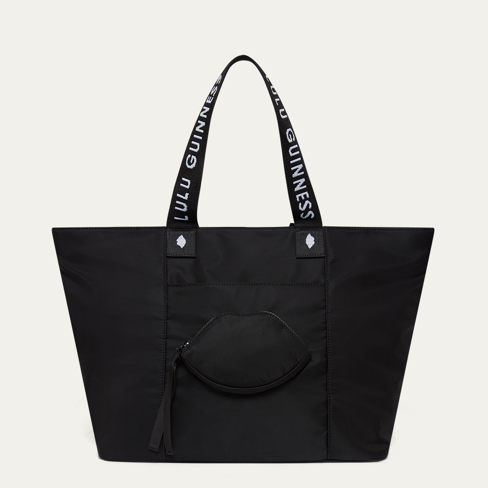 Black tote bag with Lulu Guinness handles and a lip-shaped pocket on a light gray background