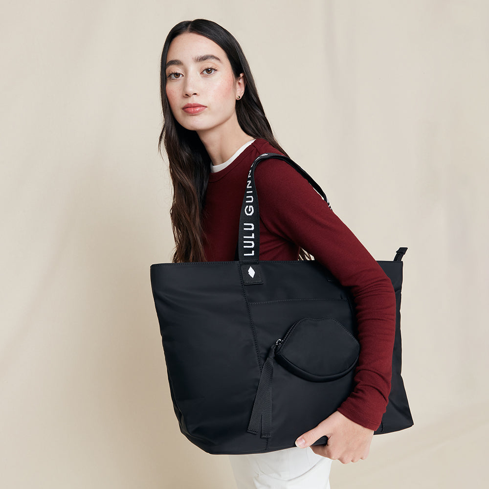 Woman holding a black bag with 'Lulu Guinness' branding against a beige background