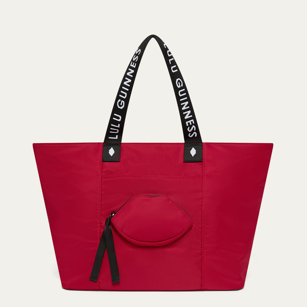 Red tote bag with black handles featuring 'Lulu Guinness' and a lip-shaped pocket on a light gray background