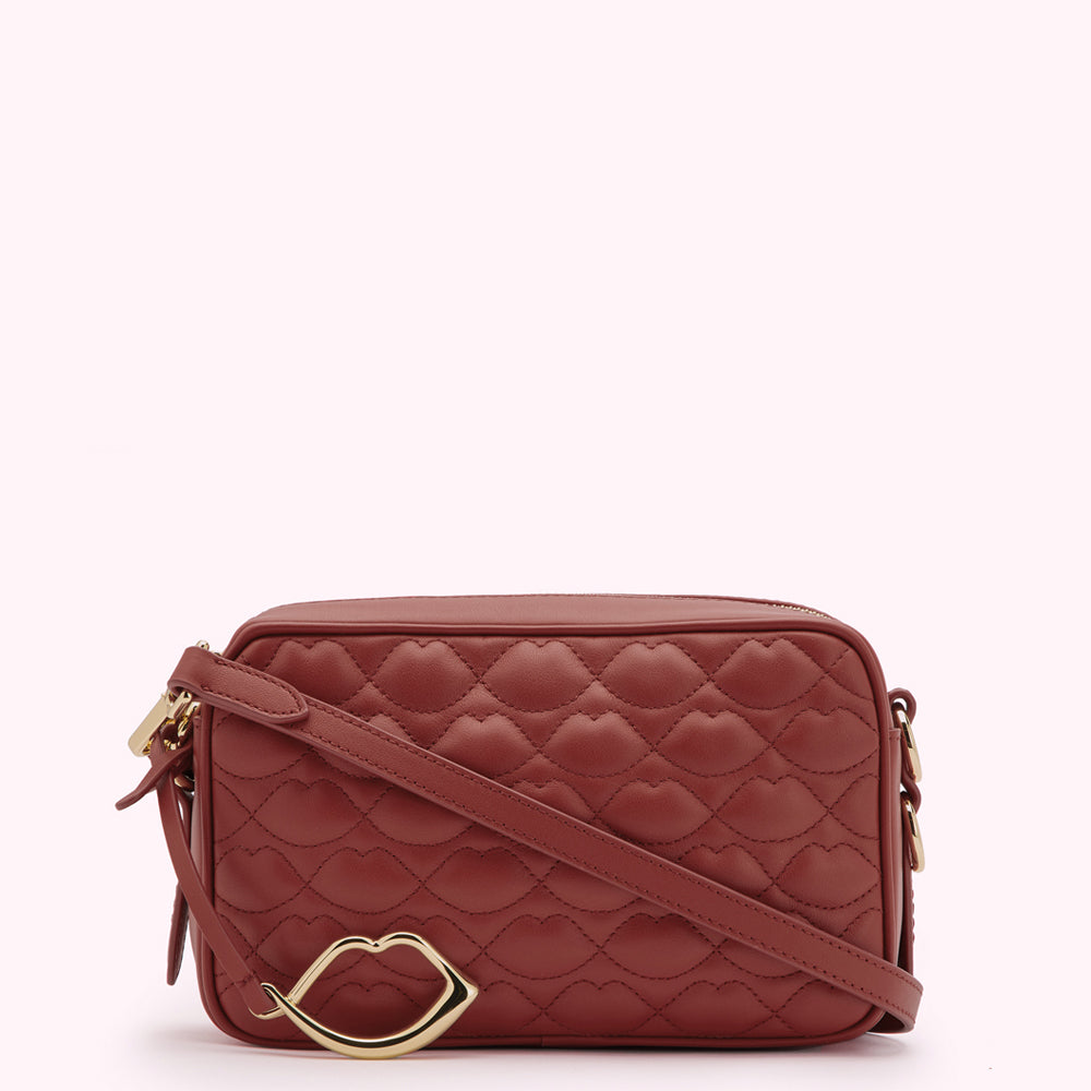 A rust-colored quilted crossbody bag with a gold lip-shaped accent.