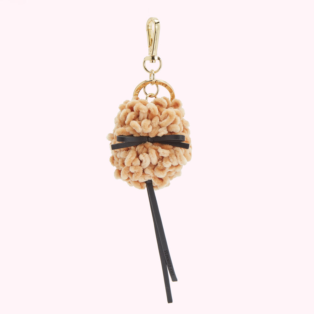 Beige pom-pom keyring with black ribbon and gold-colored hardware.
