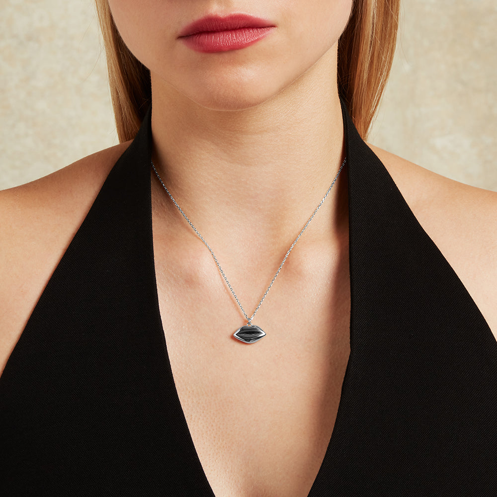 Necklace with a lip-shaped pendant worn by a person against a neutral background
