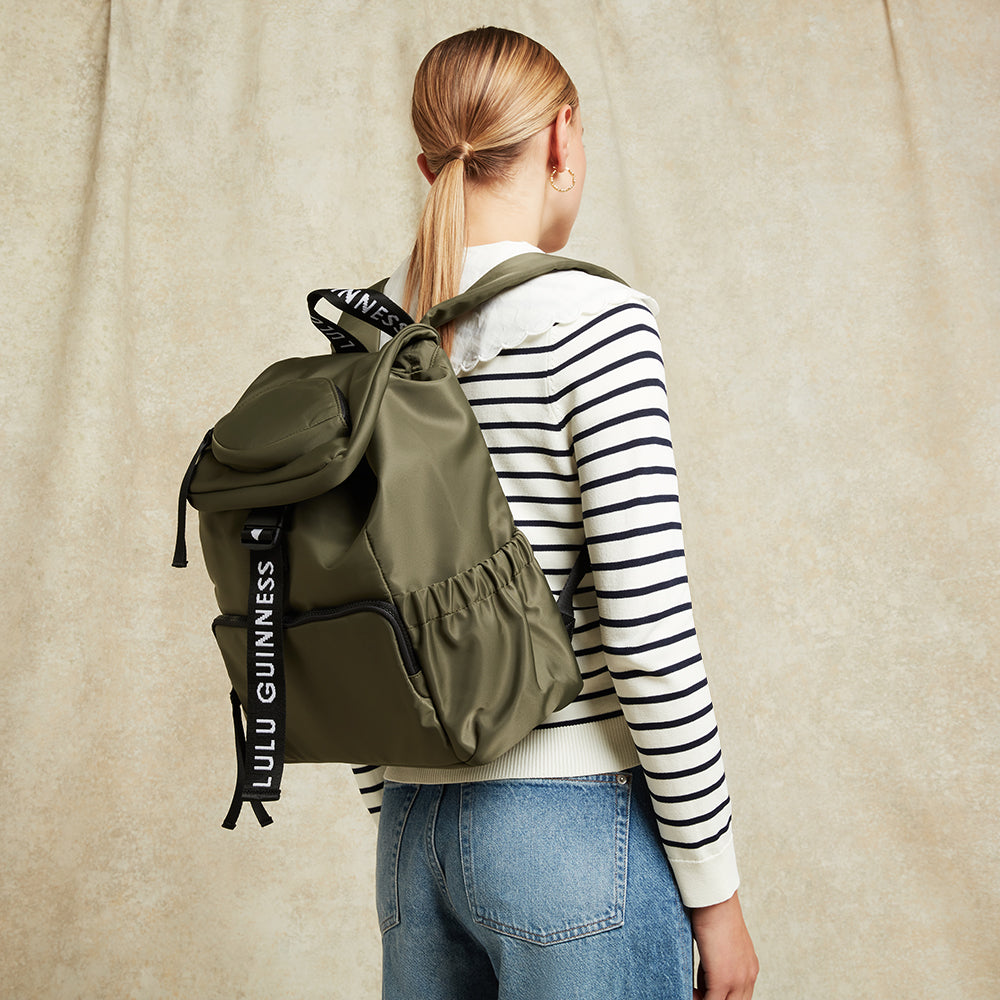 Person wearing a green backpack with Lulu Guinness strap on a beige background