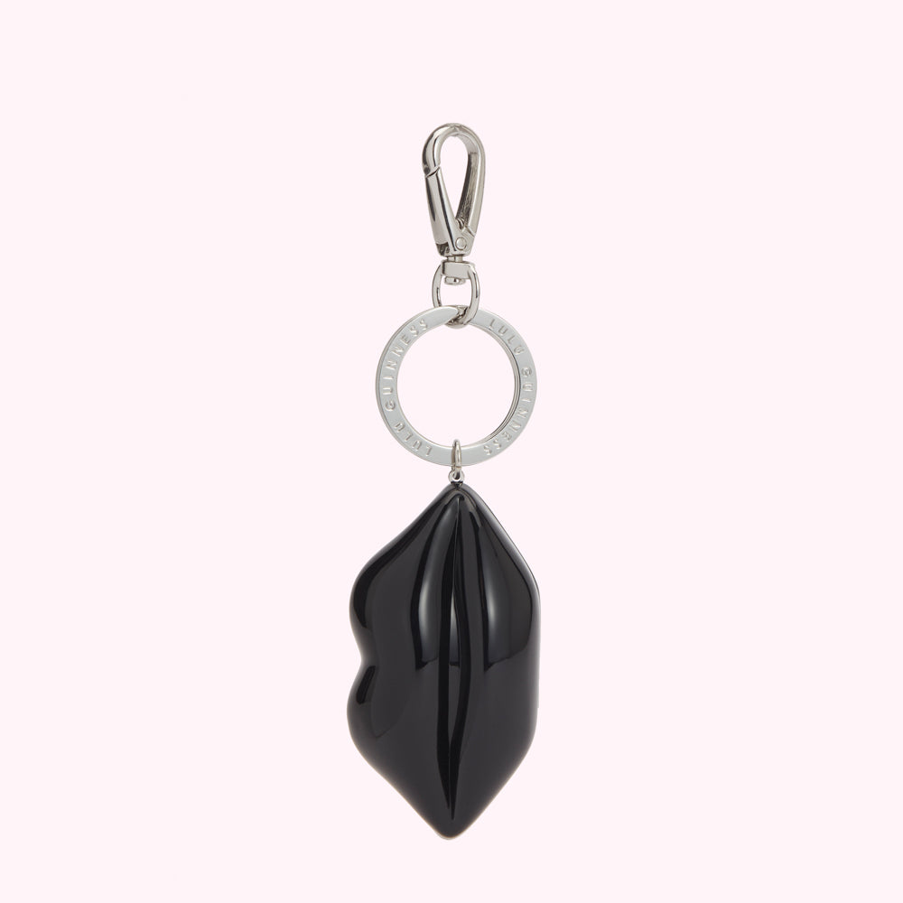 Close-up of a Lulu Guinness black tote bag with a red lip print and pearl detailing, featuring a lip-shaped keychain charm.