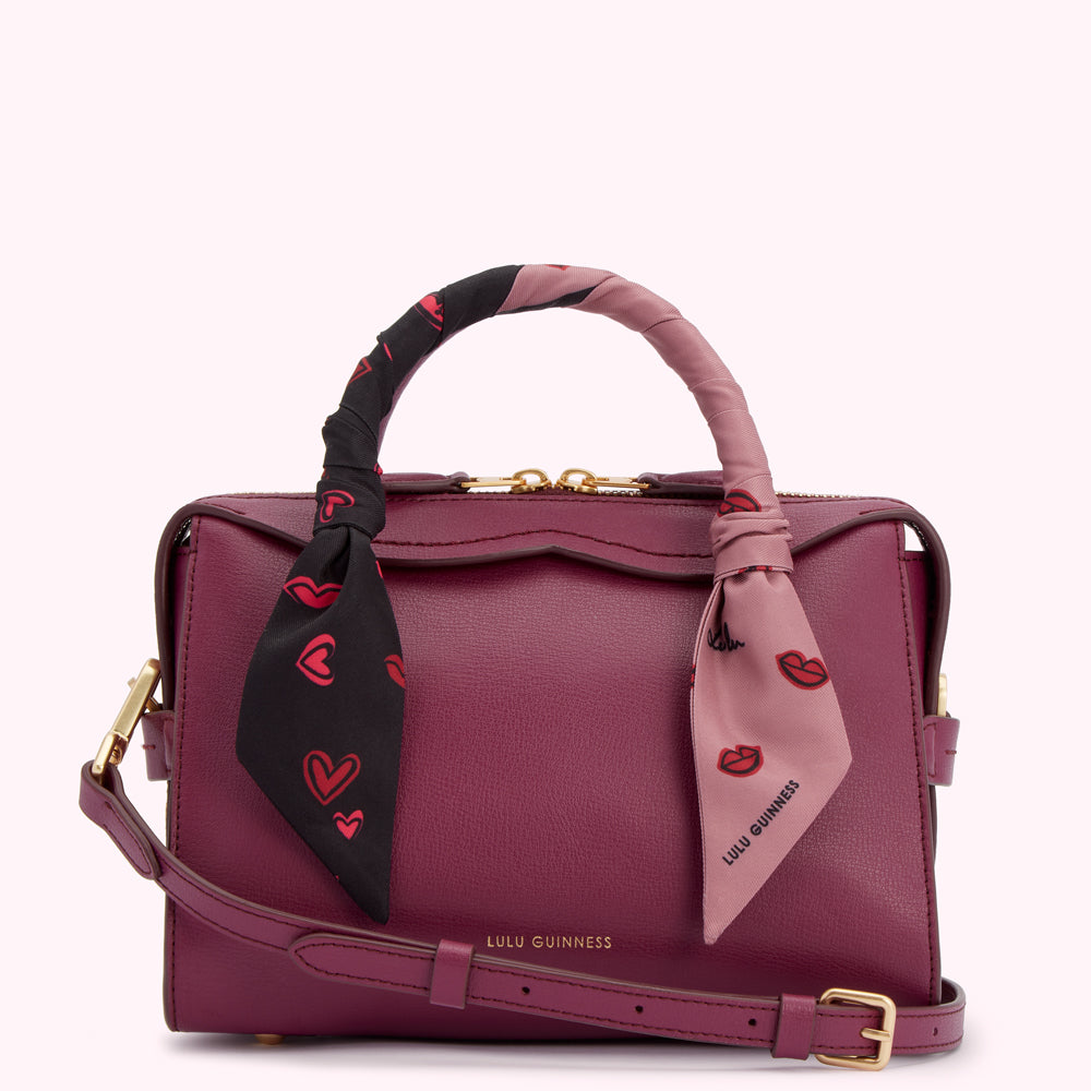 Burgundy Lulu Guinness satchel with a black and pink lips and hearts patterned scarf wrapped around the handle.