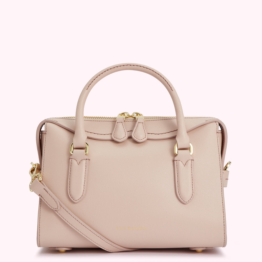A blush pink leather handbag with gold hardware and a detachable shoulder strap.
