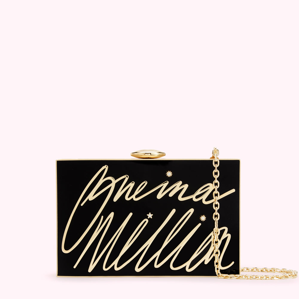 Black rectangular clutch with gold lettering that says "One in a Million" and small gold stars. A gold chain is attached.