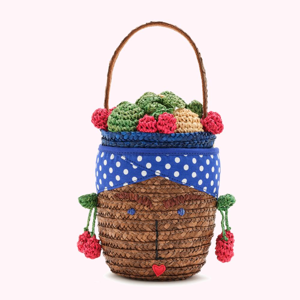 Brown woven straw handbag shaped like a face, with a blue polka dot headband, and crocheted fruit accents.