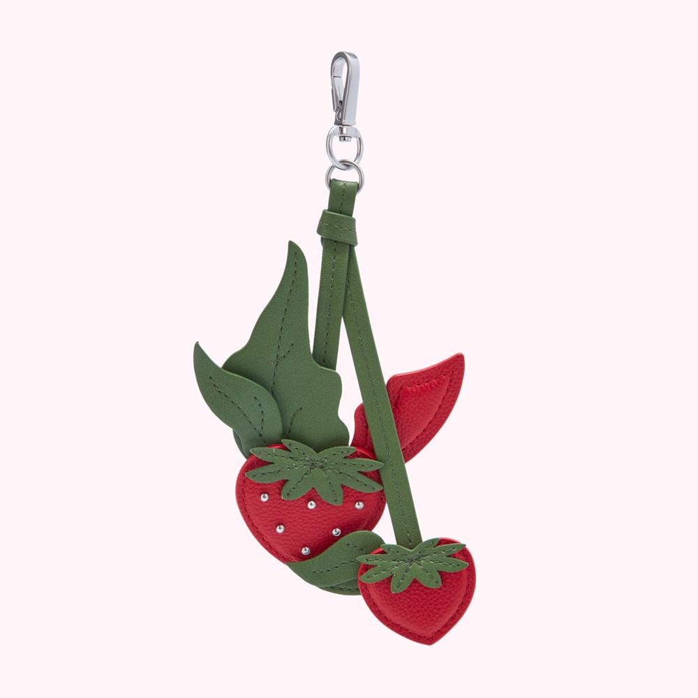 Red and green leather strawberry keychain on a white background.