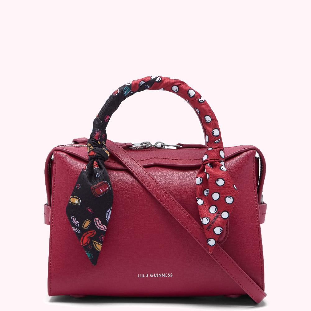 Crimson red Lulu Guinness satchel with a black and white patterned scarf wrapped around the handle.