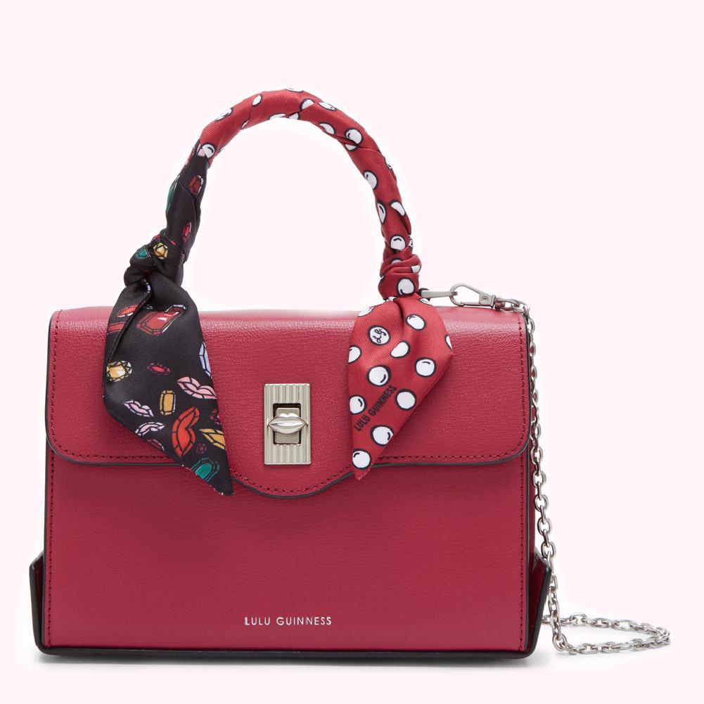 Crimson red Lulu Guinness satchel with a detachable chain strap and a patterned silk scarf adorning the handle.