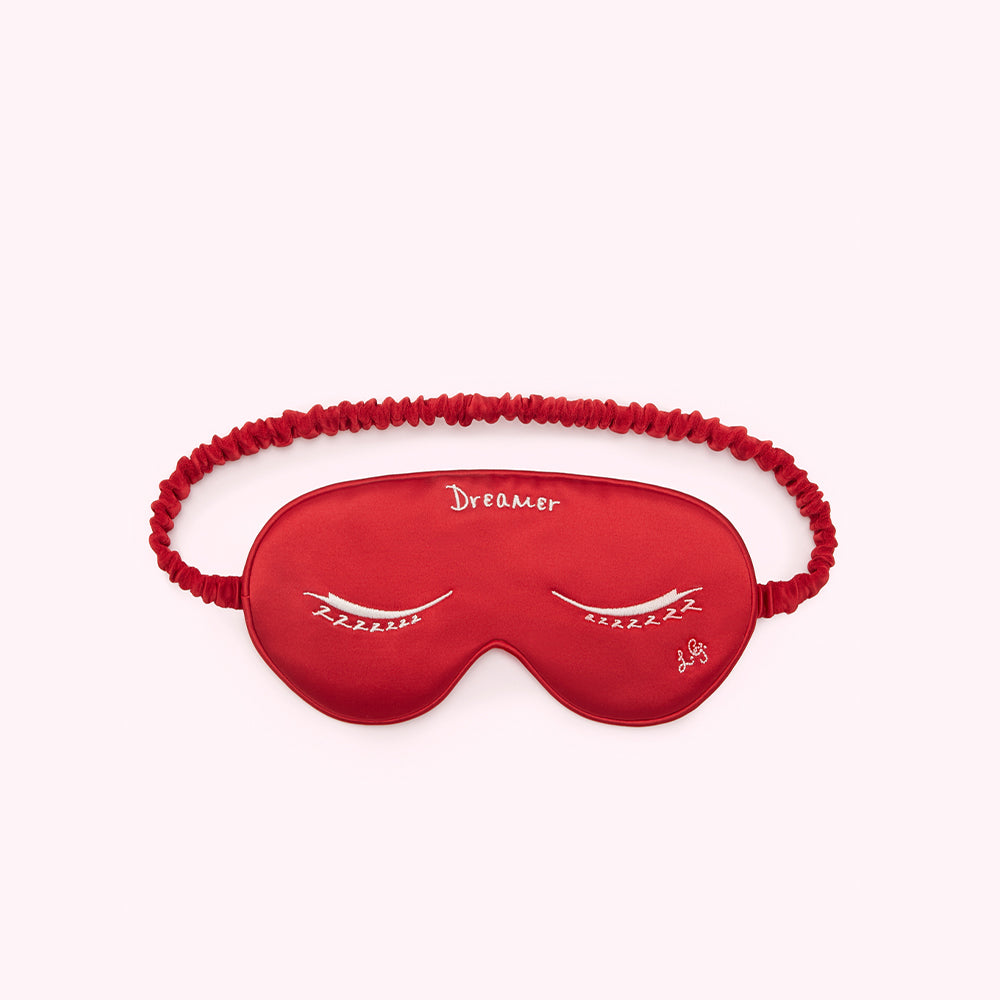 Red silk sleep mask with embroidered closed eyes and the word "Dreamer".