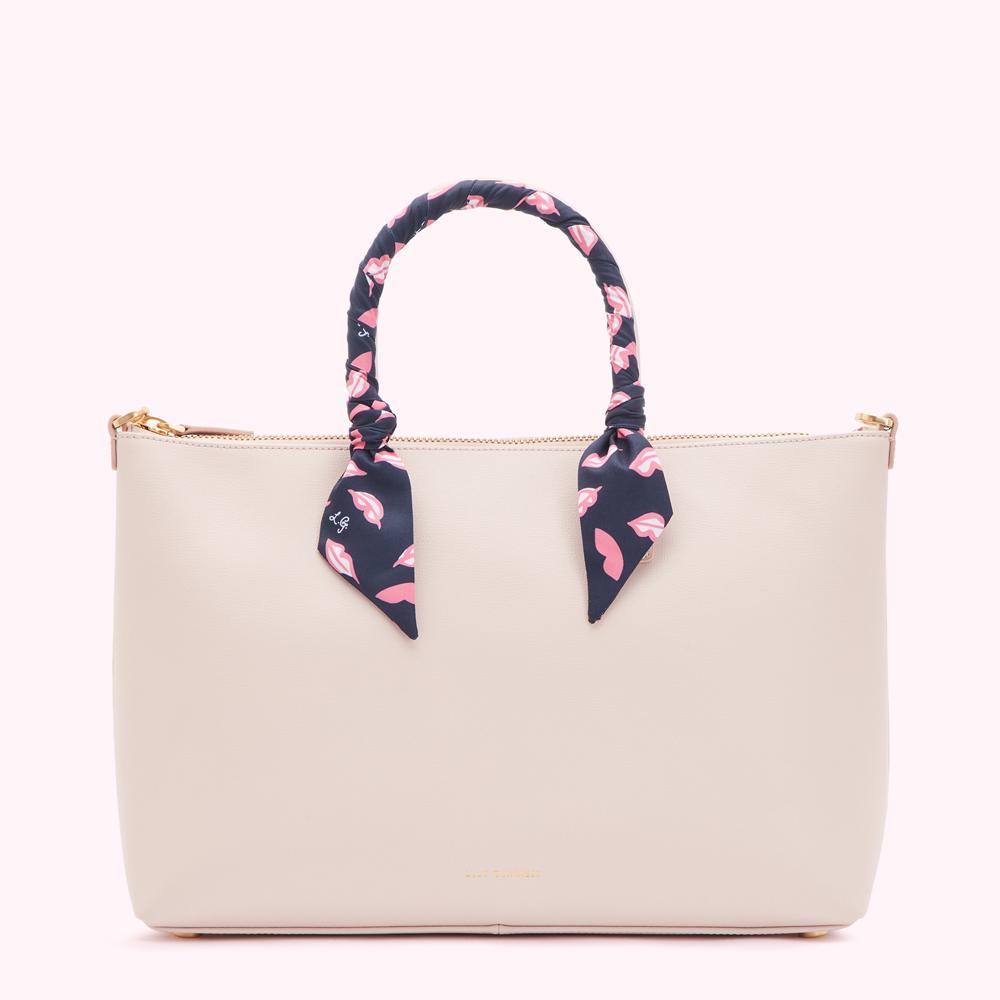 Beige tote bag with a navy blue and pink lip print scarf wrapped around the handles.