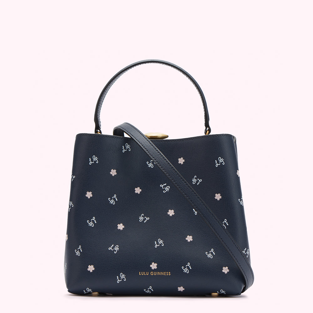 Navy blue Lulu Guinness bucket bag with a light-grey floral and logo pattern, gold clasp and strap.
