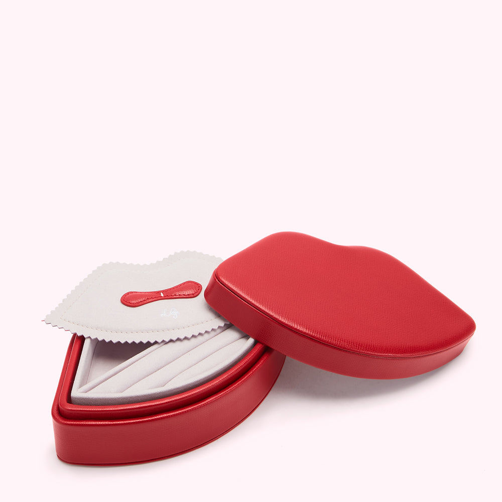 Red lip-shaped jewelry box open to reveal pink velvet interior and cleaning cloth.