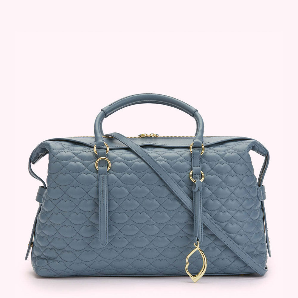 Dusty blue quilted handbag with gold-tone hardware and a detachable shoulder strap. The quilting pattern is a repeating lip design.