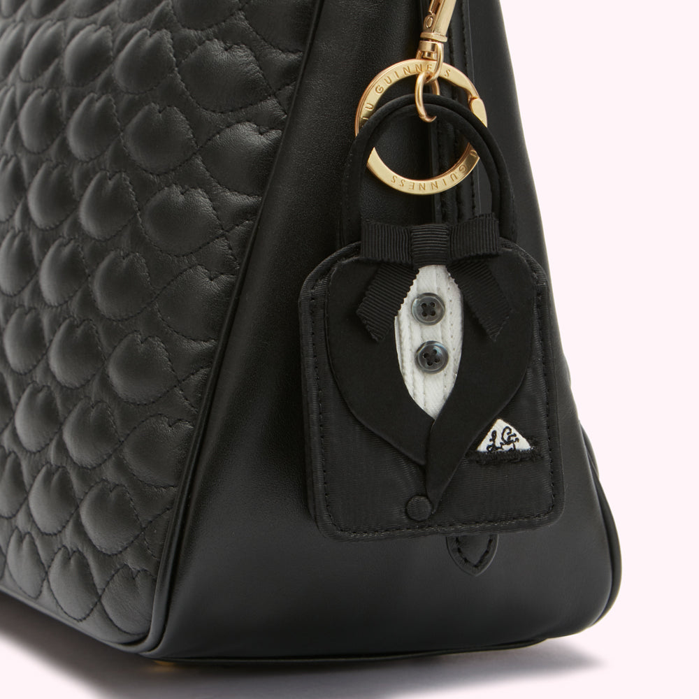 Close-up of a black quilted leather handbag with a tuxedo-shaped keychain attached.
