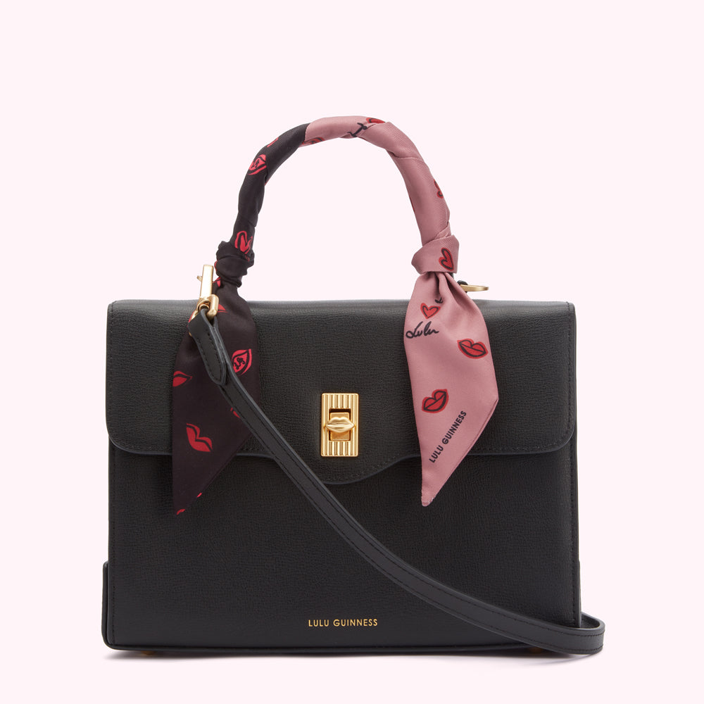 Black Lulu Guinness satchel bag with a pink and black lip-print scarf wrapped around the handle.