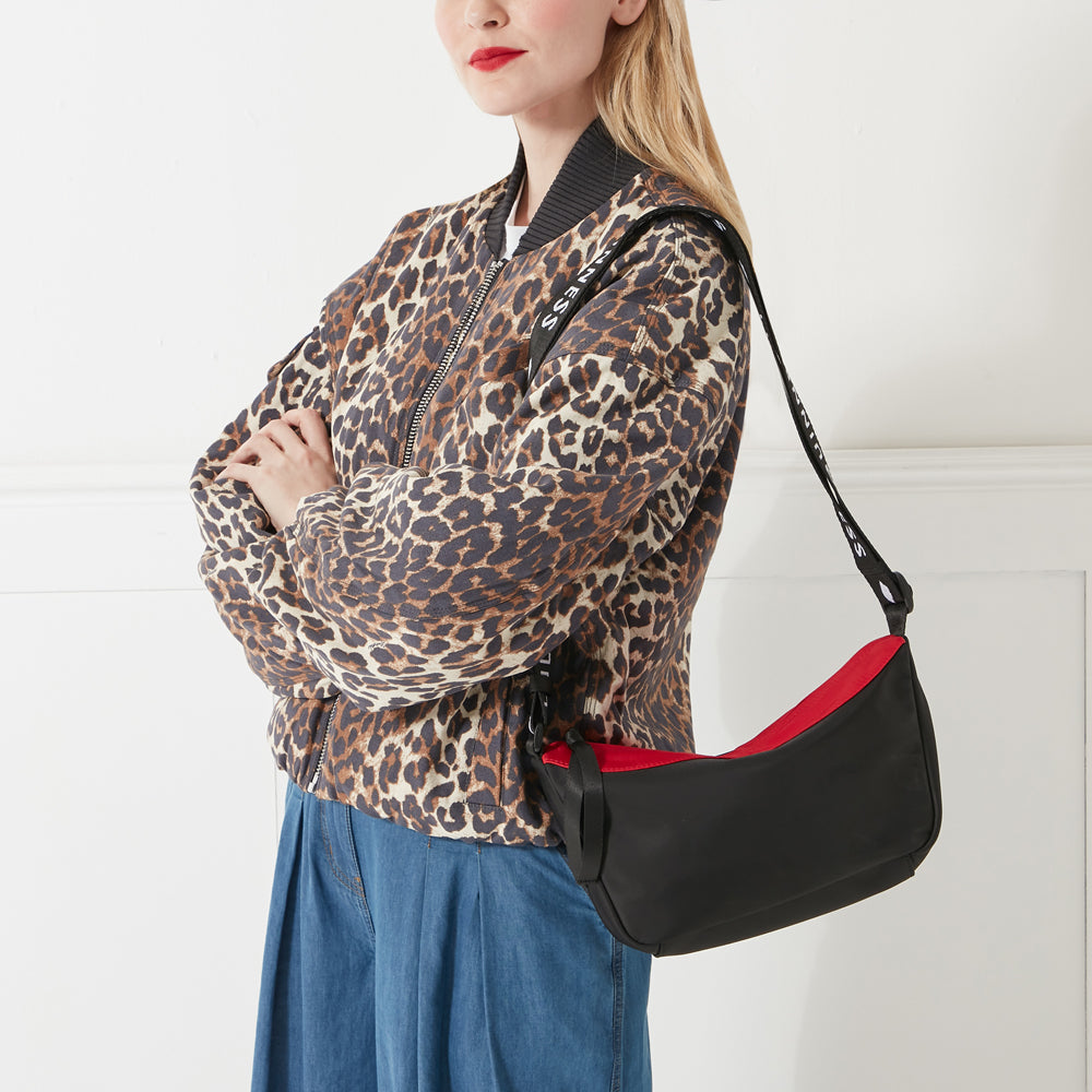 Woman wearing a leopard print jacket and denim jeans, with a black crossbody bag featuring a black and white "Lulu Guinness" logo strap. The background is white.
