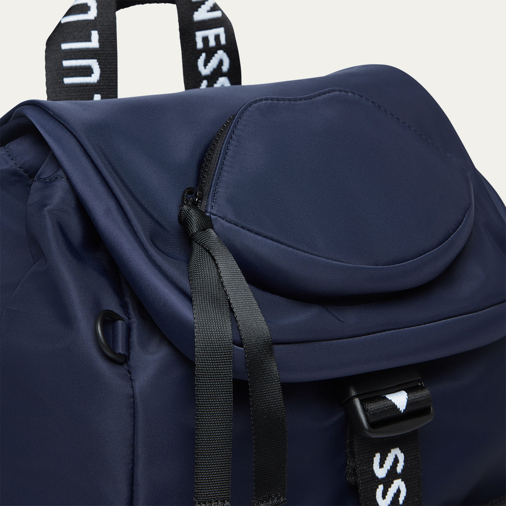 Navy blue backpack with black 'Lulu Guinness' branded straps on a light gray background