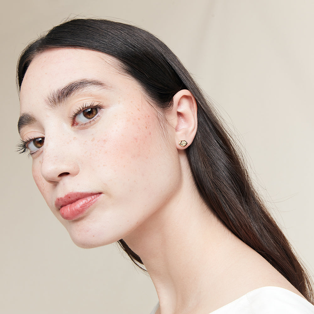 Close-up of a woman wearing a gold  lip shaped stud earring against a neutral background