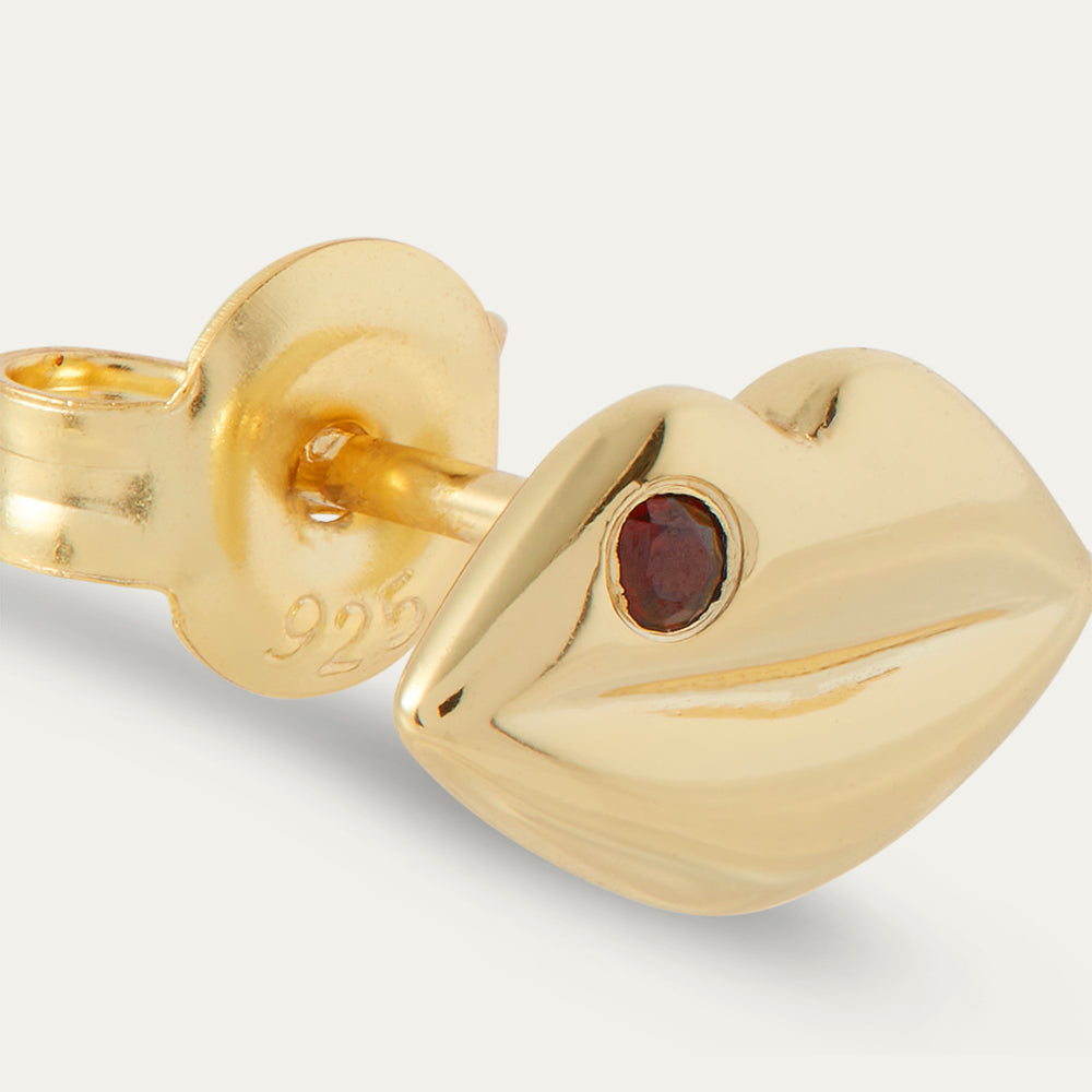 Gold earring with a red gemstone on a light gray background