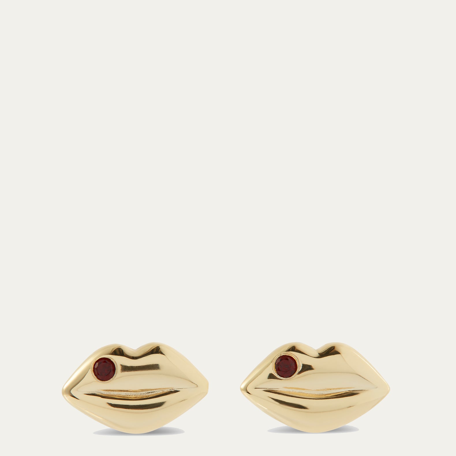 Gold lip-shaped earrings with red stones on a white background