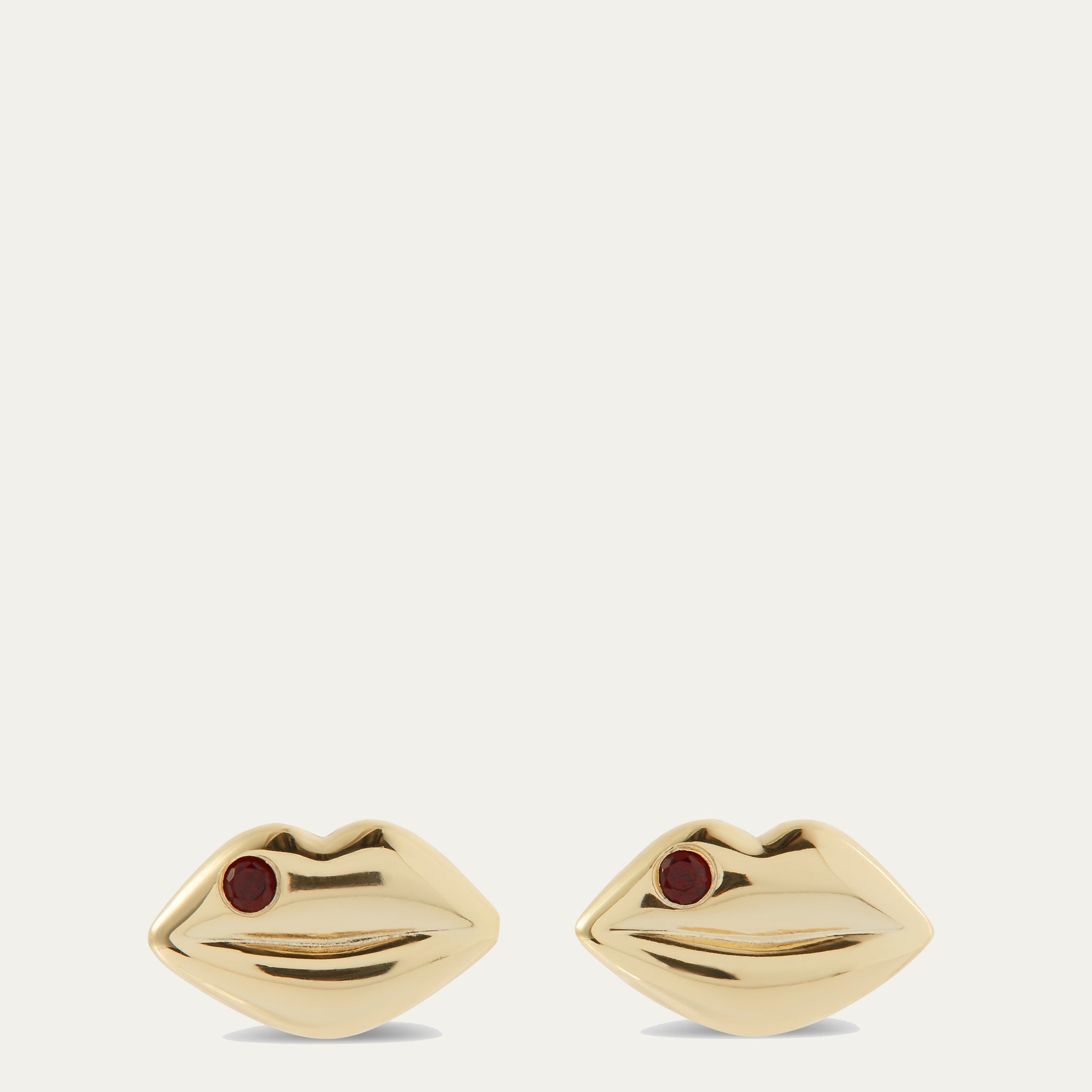 Gold lip-shaped earrings with red stones on a white background