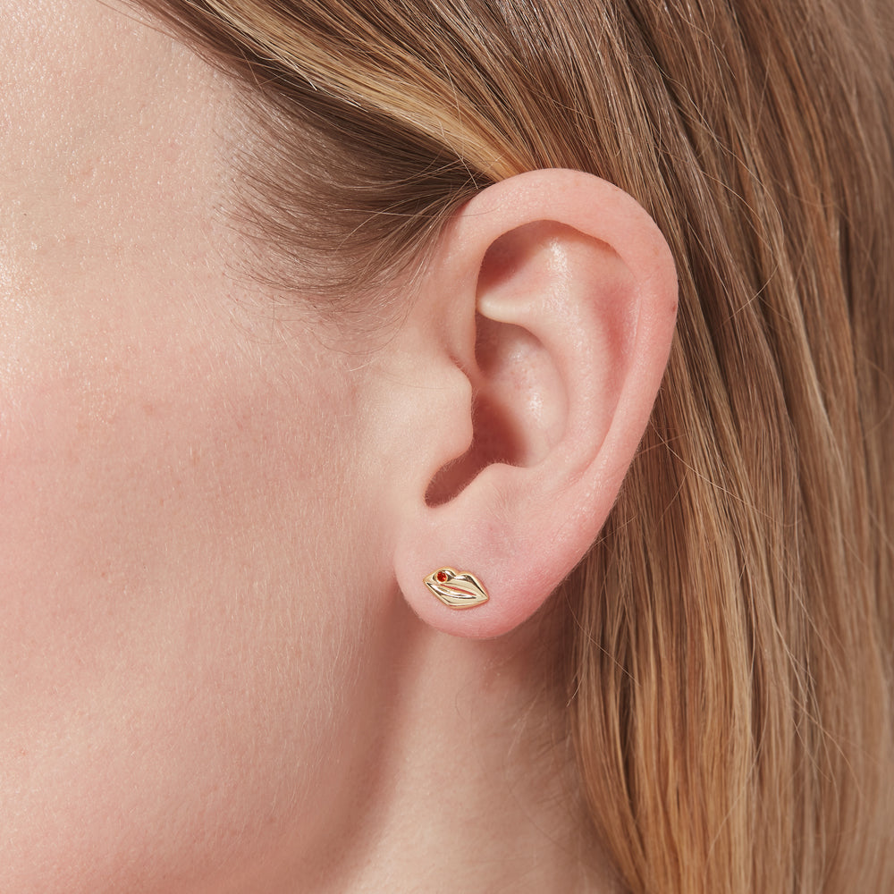 Lip-shaped gold earring worn on a person's ear with a neutral background