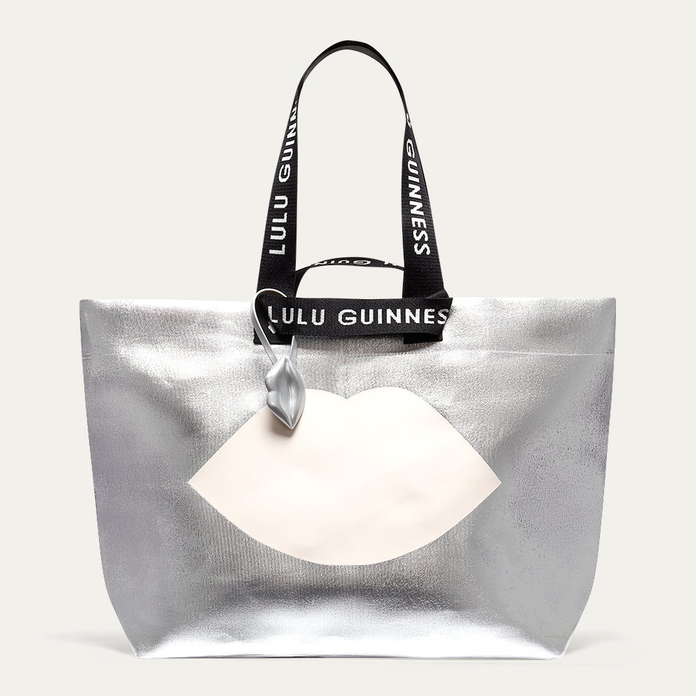 Silver tote bag with a white lip design and Lulu Guinness strap on a light gray background