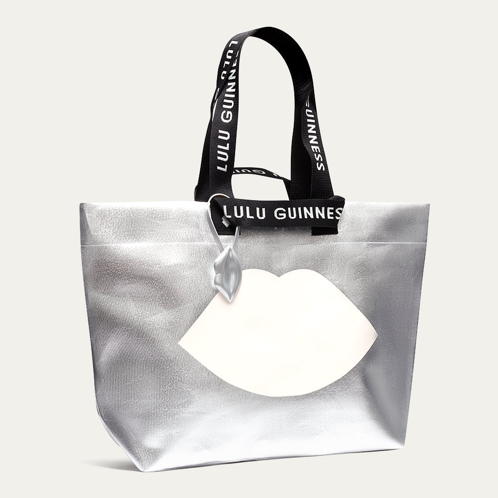 Silver tote bag with black handle featuring 'Lulu Guinness' branding on a white background.