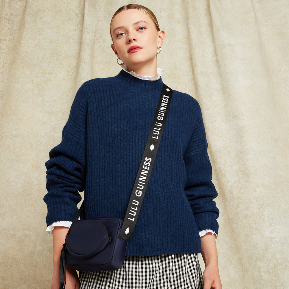 Woman wearing a navy sweater with a matching bag featuring 'Lulu Guinness' on a beige background