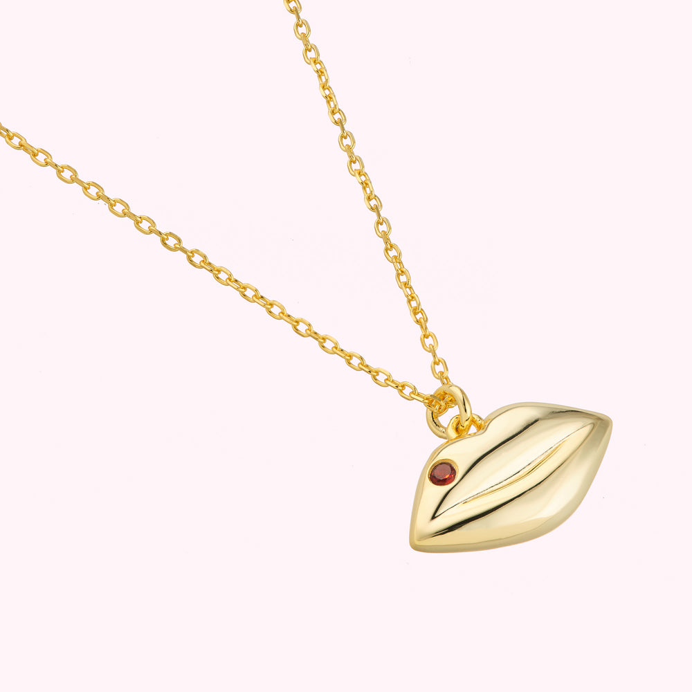 Close up details of 14K gold plated sterling silver solid lip pendant charm on a chain featuring a inset Ruby precious stone.