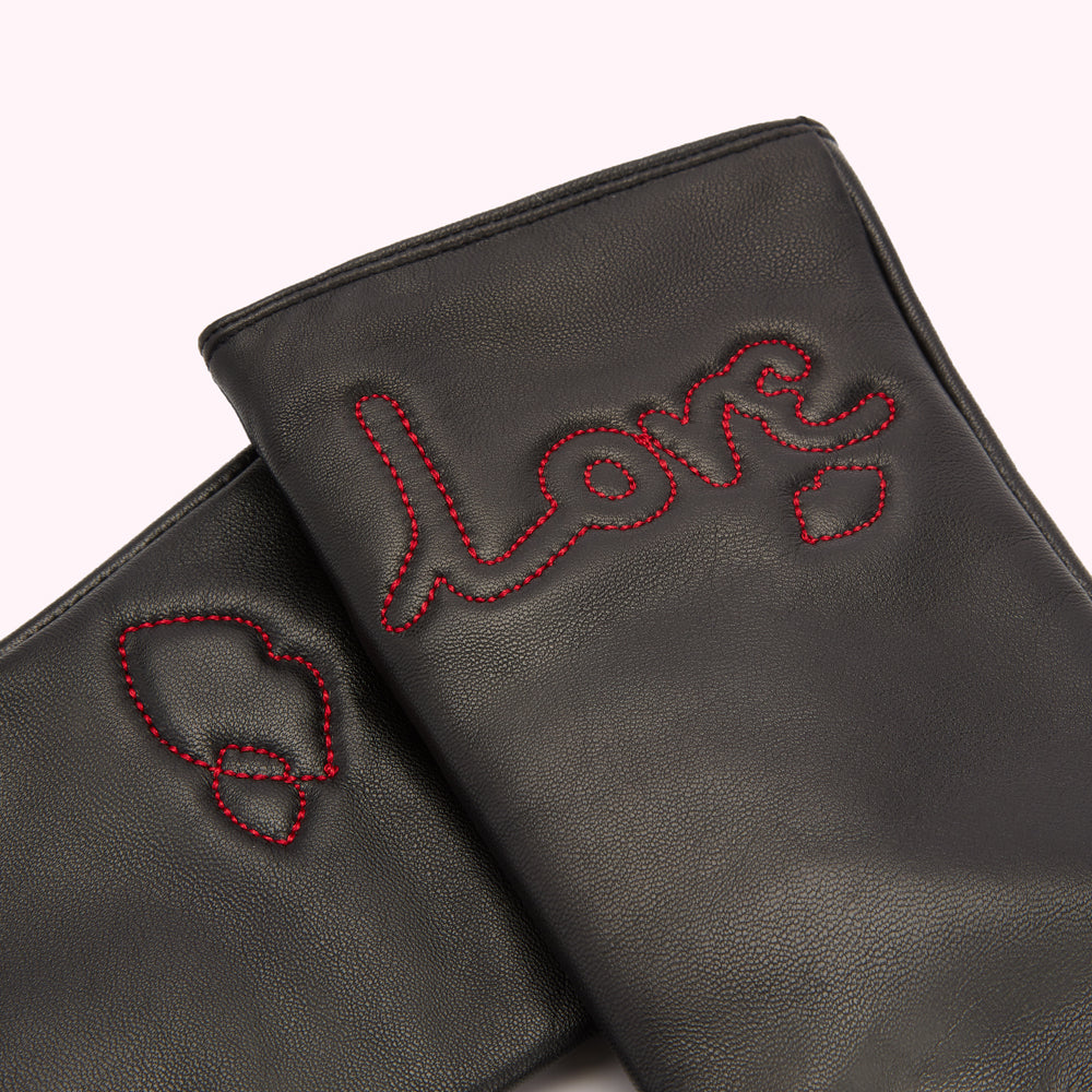 Close-up of a pair of black leather gloves with "love" embroidered in red thread.