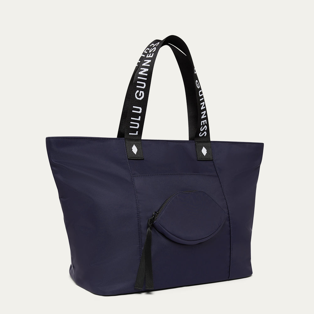 Navy tote bag with black handles featuring 'Lulu Guinness' branding on a light gray background.