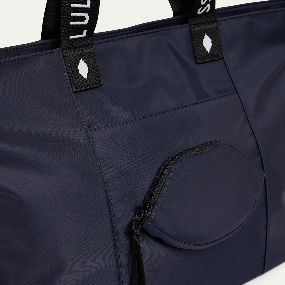 Navy blue tote bag with a lip-shaped pocket and black straps on a light gray background
