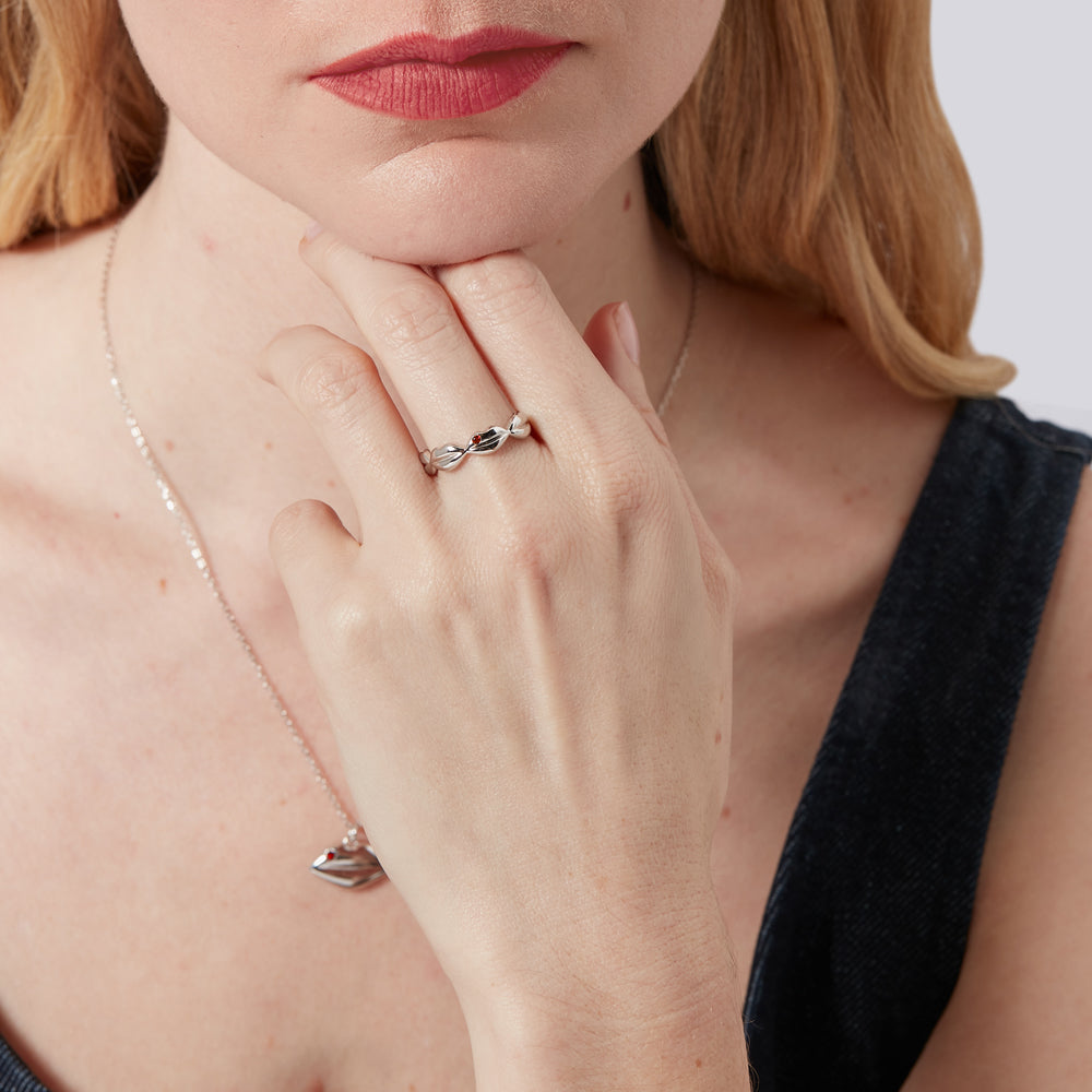 Model wearing red lipstick holding hand to chin and wearing a sterling silver lip Luna ring with inset ruby details. 