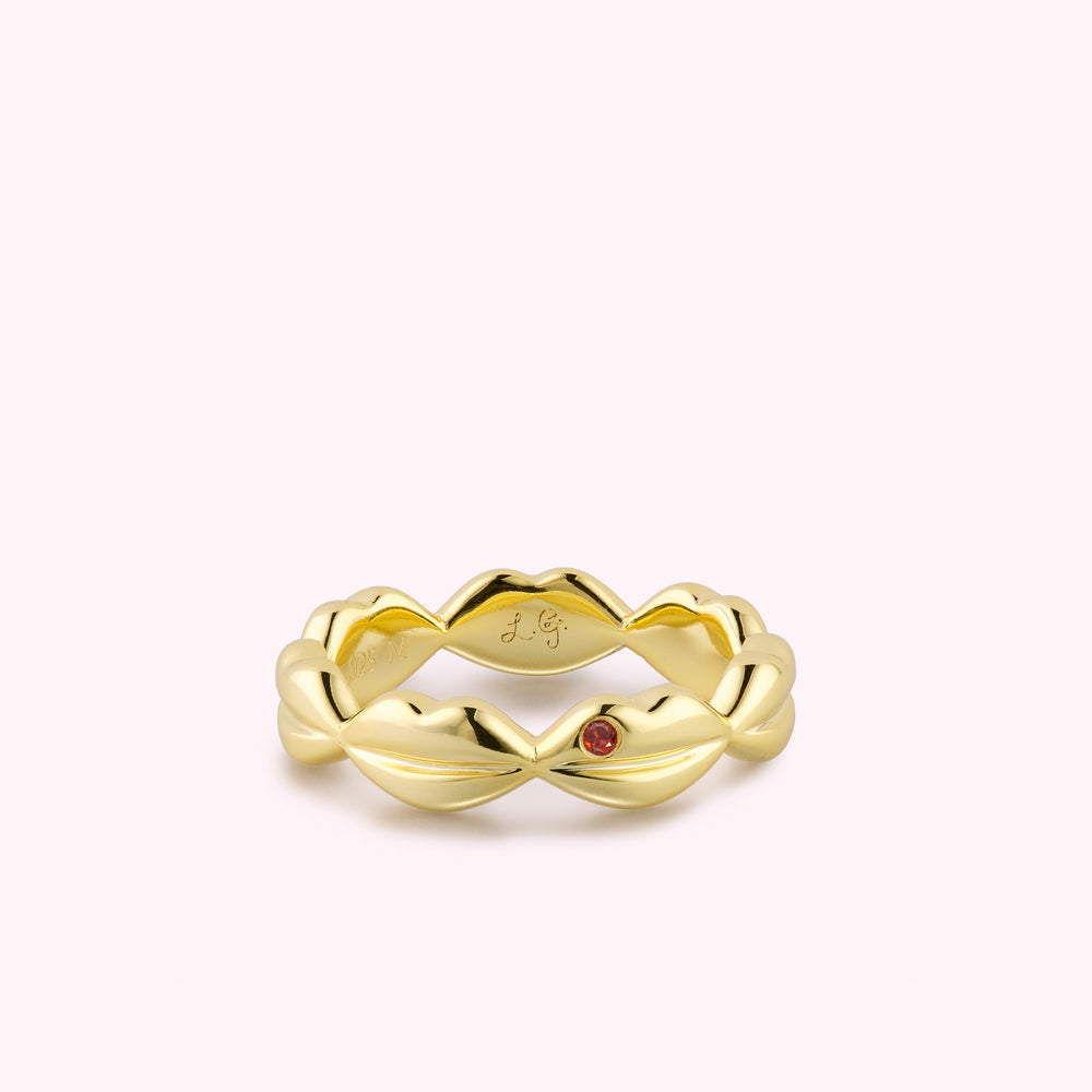 Gold lip shape ring with inset ruby stone and engraved brand logo.