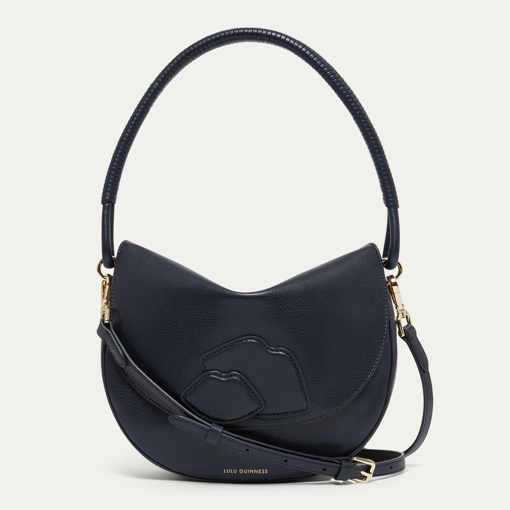 Navy leather handbag with a corded handle, crossbody strap with gold buckle and lip details on a light gray background