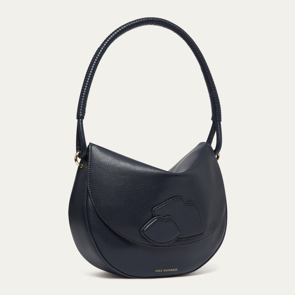 Navy blue leather shoulder bag with lip details and a corded handle on a light grey background