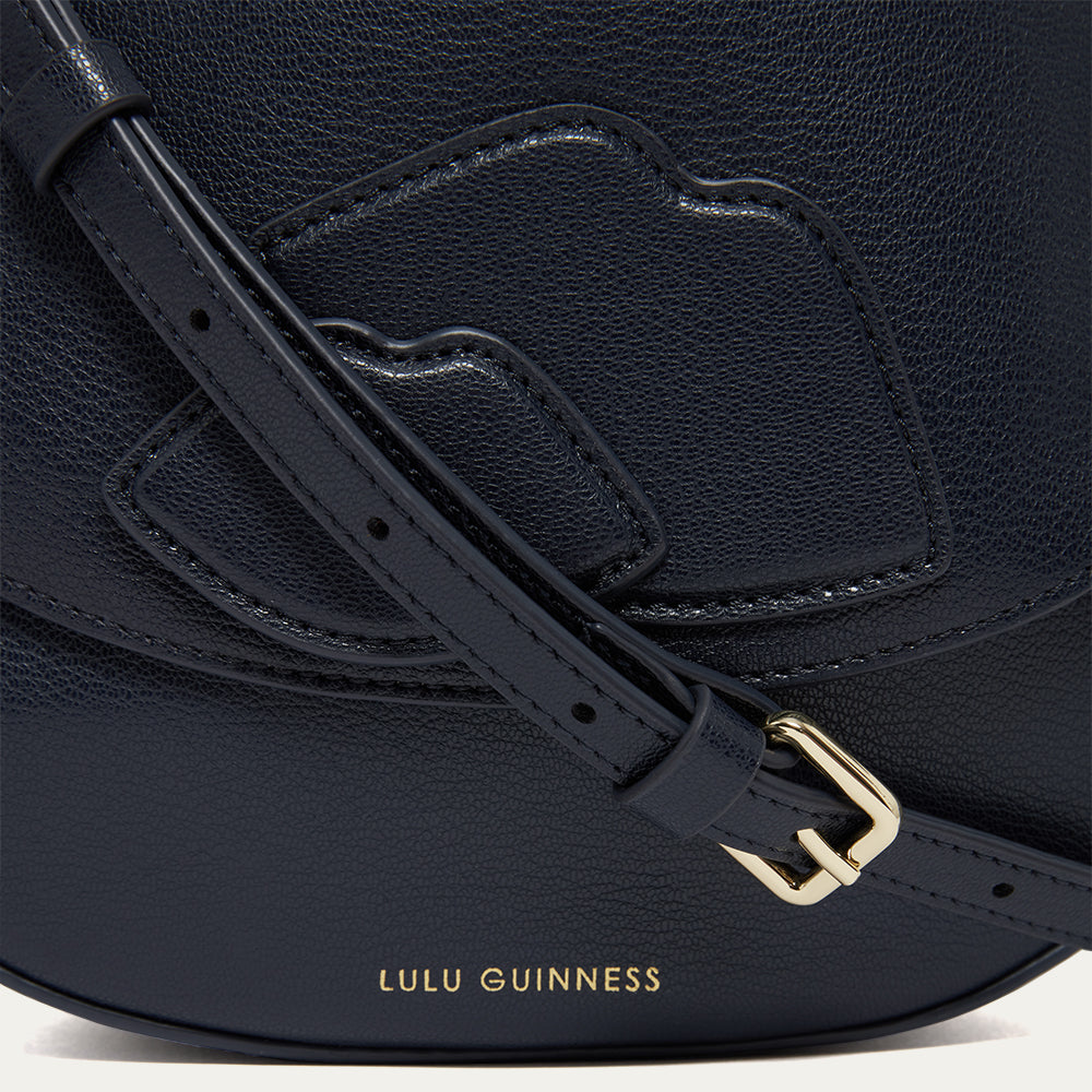 Detail of lip details on a navy blue leather  handbag with a strap with a gold buckle, featuring the 'Lulu Guinness' logo.