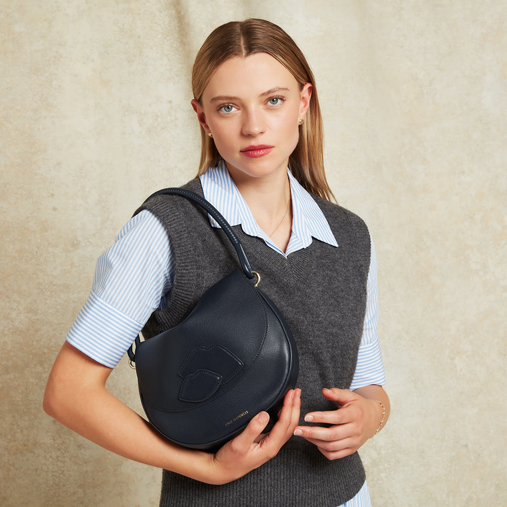 Woman holding a navy leather shoulder bag against a beige background