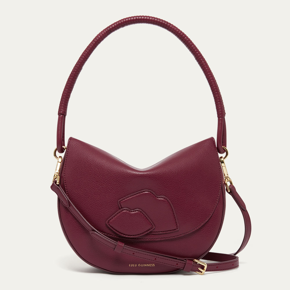 Burgundy leather handbag with lip details, a corded leather shoulder strap and crossbody strap on a light grey background
