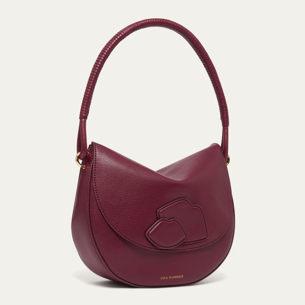 Burgundy leather shoulder bag with a corded handle and lip details on a light grey background
