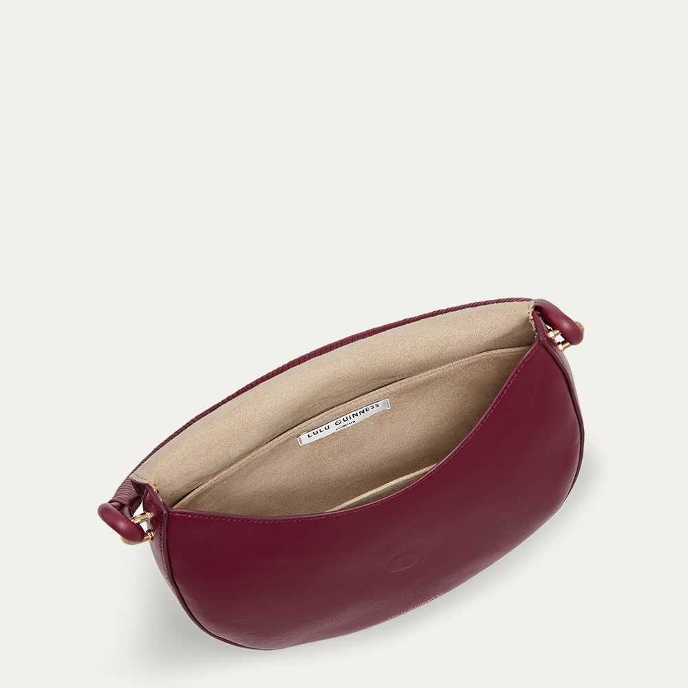 Inside image of a burgundy leather handbag with a beige interior on a light gray background