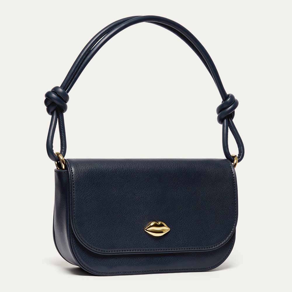 Navy blue leather shoulder bag with a gold lip on the front and a knotted shoulder strap on a light gray background