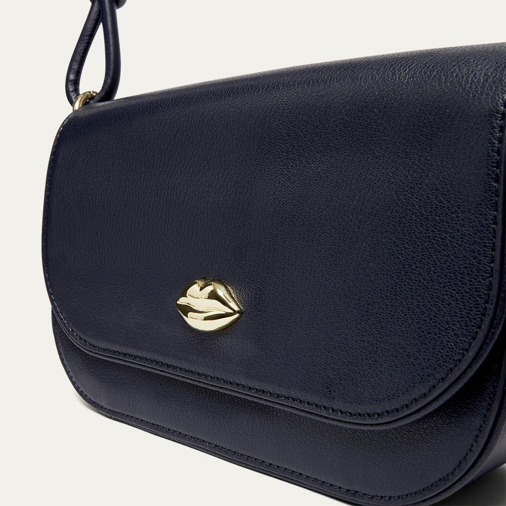 Navy blue leather shoulder bag with a gold lip on the front on a light gray background